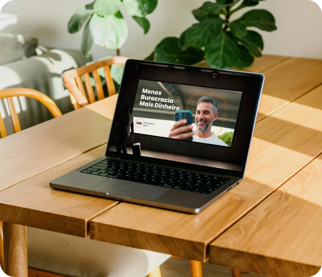 Notebook aberto exibindo tela com homem sorrindo e texto "Menos Burocracia Mais Dinheiro