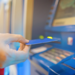 Mão insere cartão em caixa eletrônico para receber benefício do INSS via Pix.